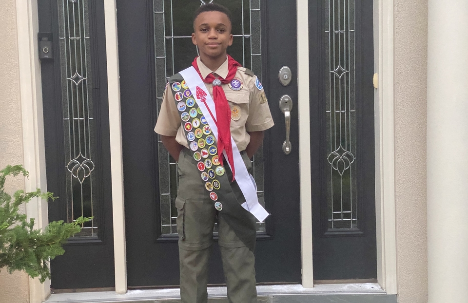 希尔·霍姆斯穿着他的童子军制服站在门前，展示着许多徽章