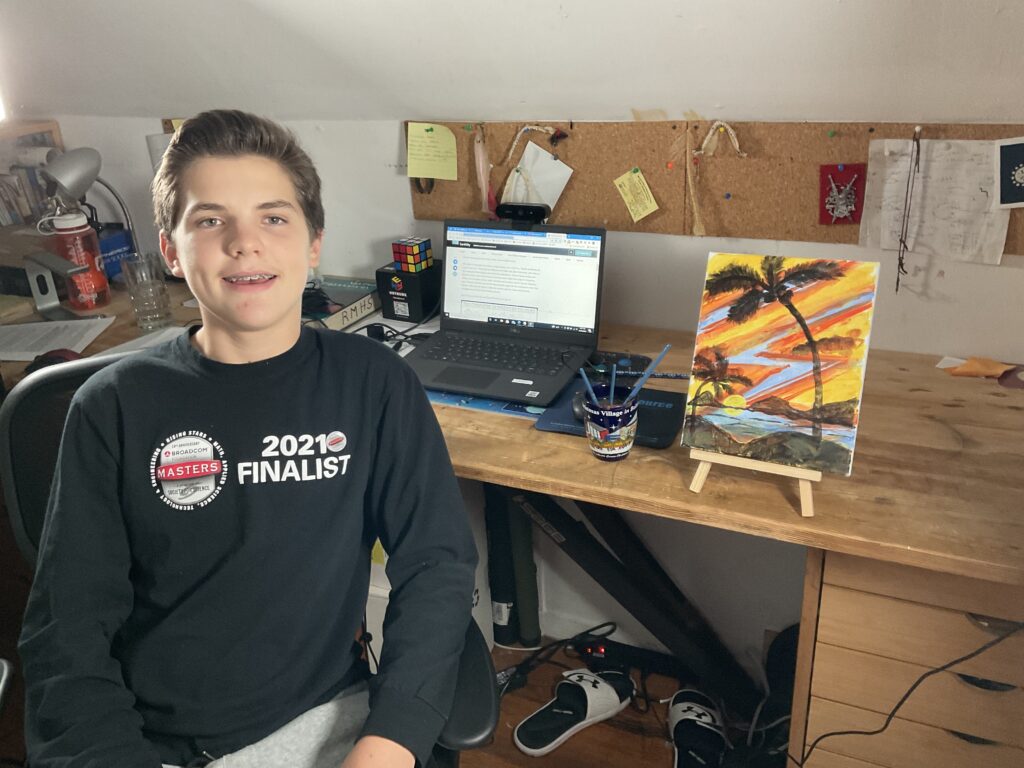 约瑟夫·西姆克（Joseph Simak）是2021年的Broadcom Masters校友，他在他的虚拟比赛中画的一幅画作在他的桌子前面摆姿势。