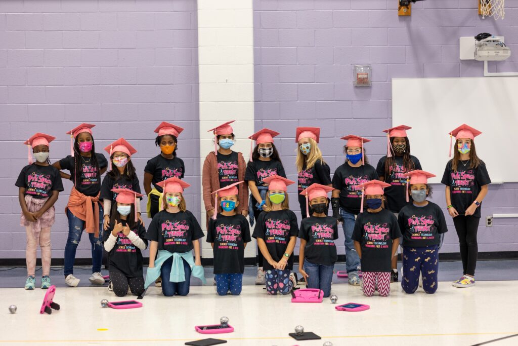 一群年轻女孩在体育馆里摆张照片，戴着粉红色的毕业帽。